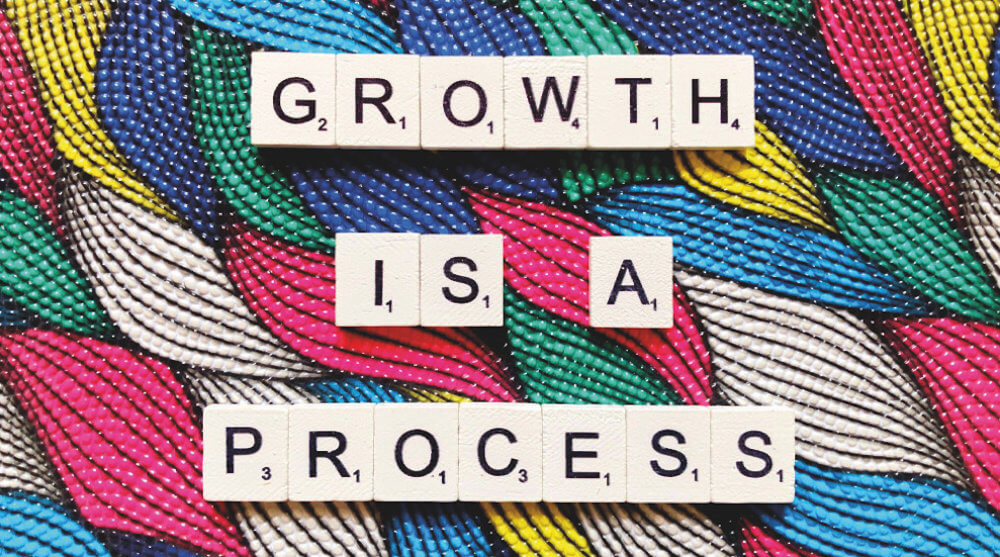 Scrabble letters spell out "growth is a process" on a colorful background.
