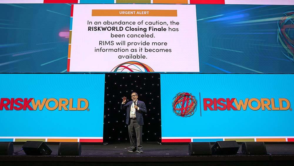 man speaking from RISKWORLD stage under sign stating closing finale is canceled