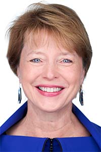 woman with short hair, blue top, dangling earrings smiling