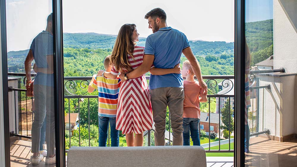father, mother, two young sons looking off hotel balcony at mountains