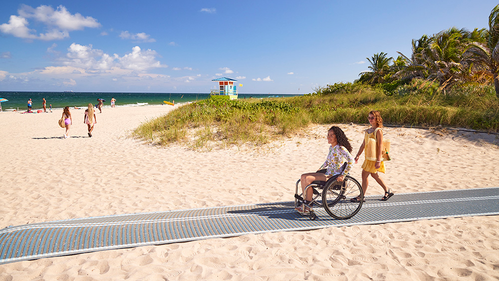 woman in wheelchair accessing the beach via a mobility mat