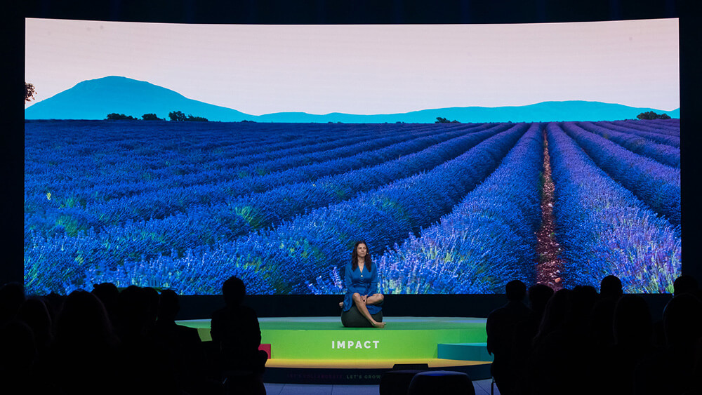 woman sitting with one leg crossed in from of giant screen showing lavender field