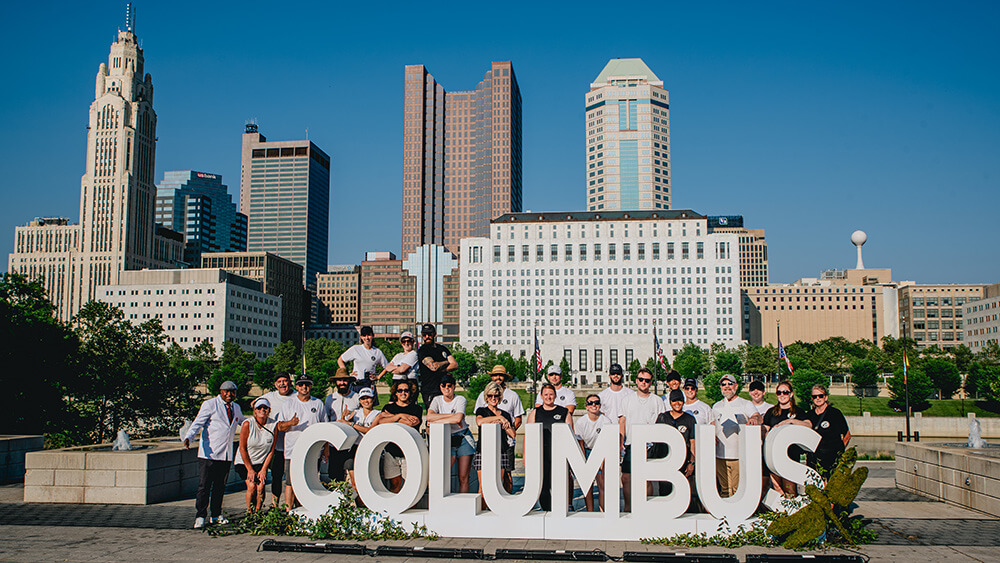 group of people behind columbus sign in front of skyline