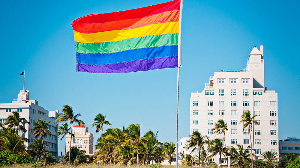 gay flag in sand in front of hotels