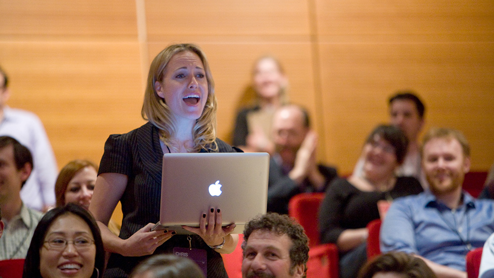 una mujer con una computadora portátil canta entre el público